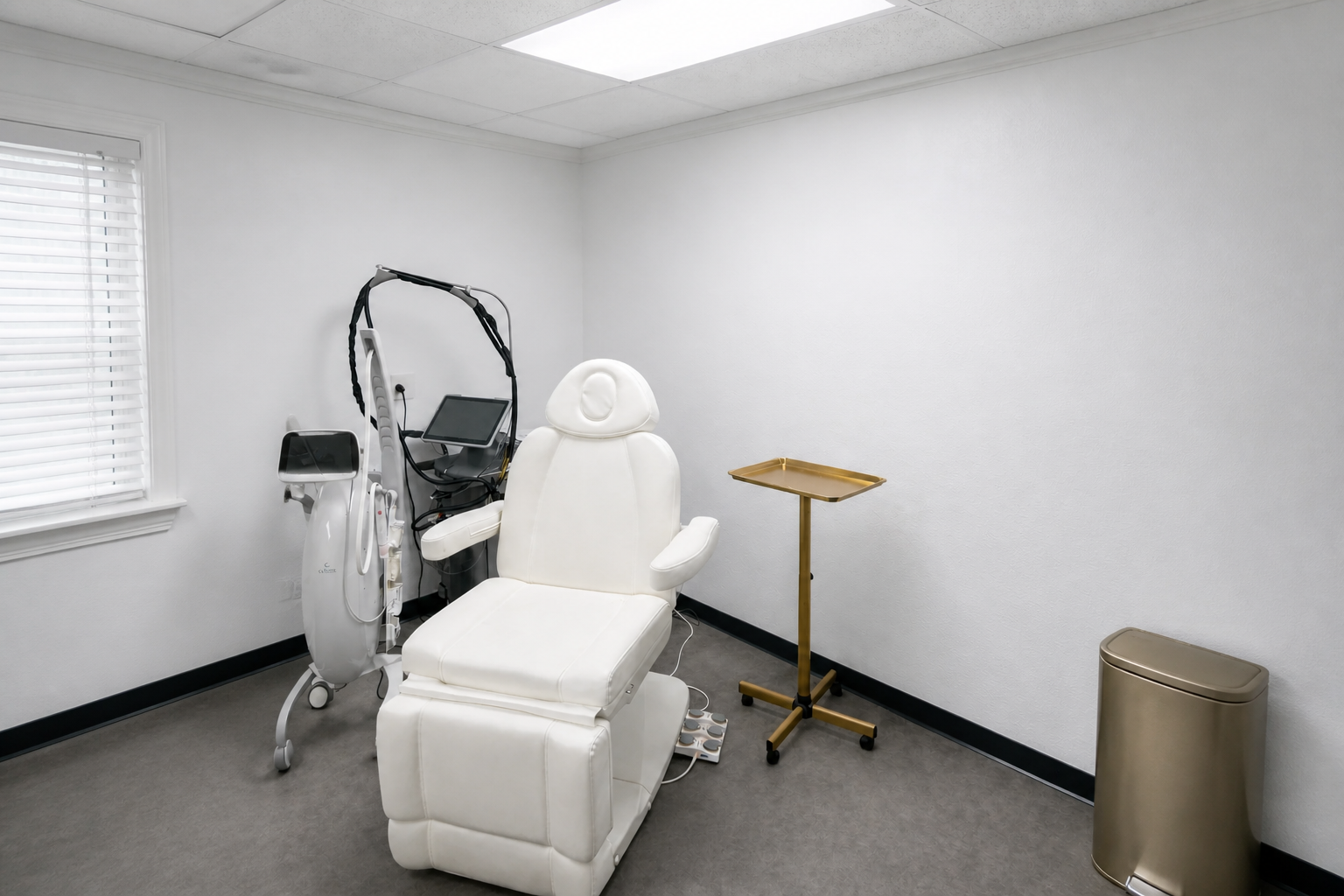 An empty treatment room with a white chair and a gold rolling tray stand. The room where the consultation happens. The questions you ask here matter more than the price list. 